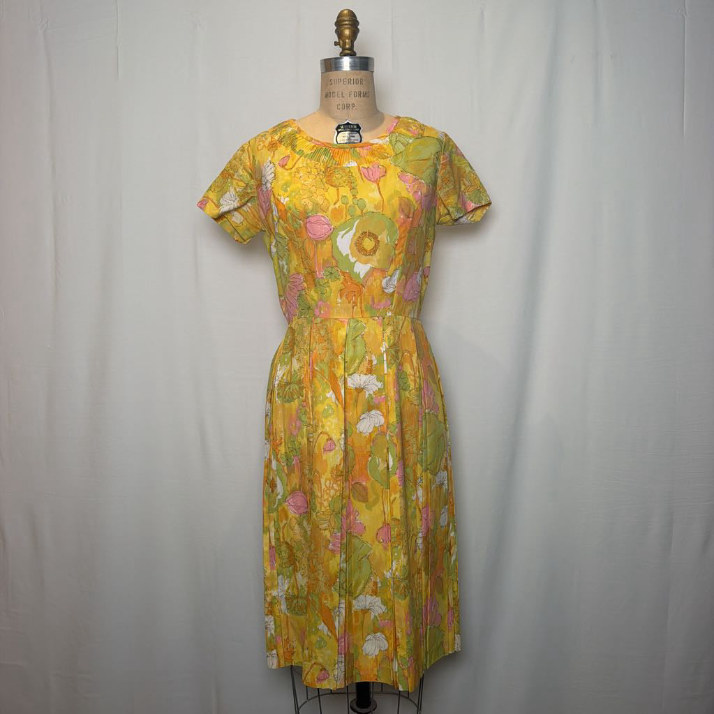 A vintage 1960s or 1970s floral print dress displayed on a dress form mannequin against a white fabric backdrop. The dress features a vibrant yellow base with pink, green, and white floral motifs.