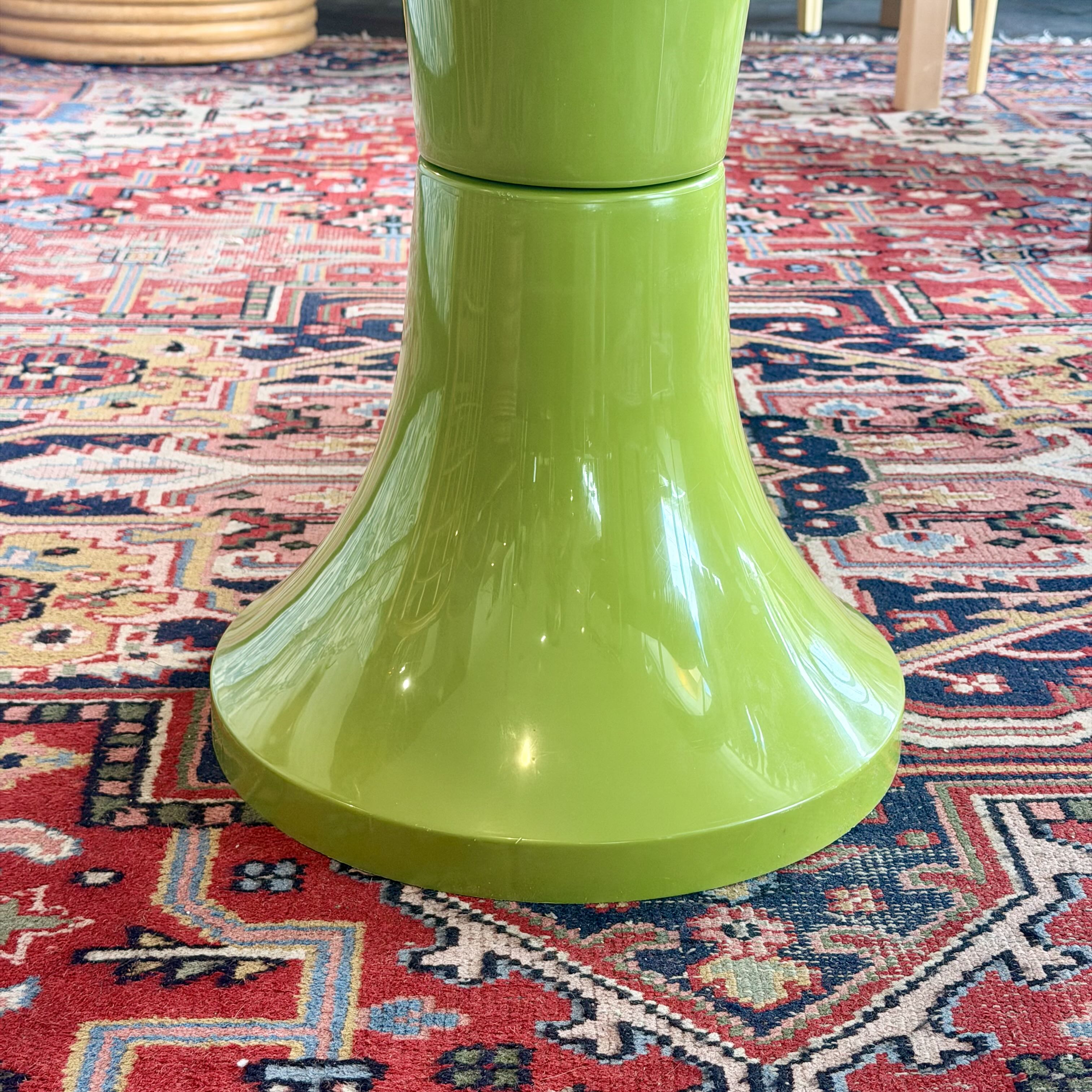 A close-up of a glossy lime green pedestal table base resting on a red and blue patterned oriental rug.