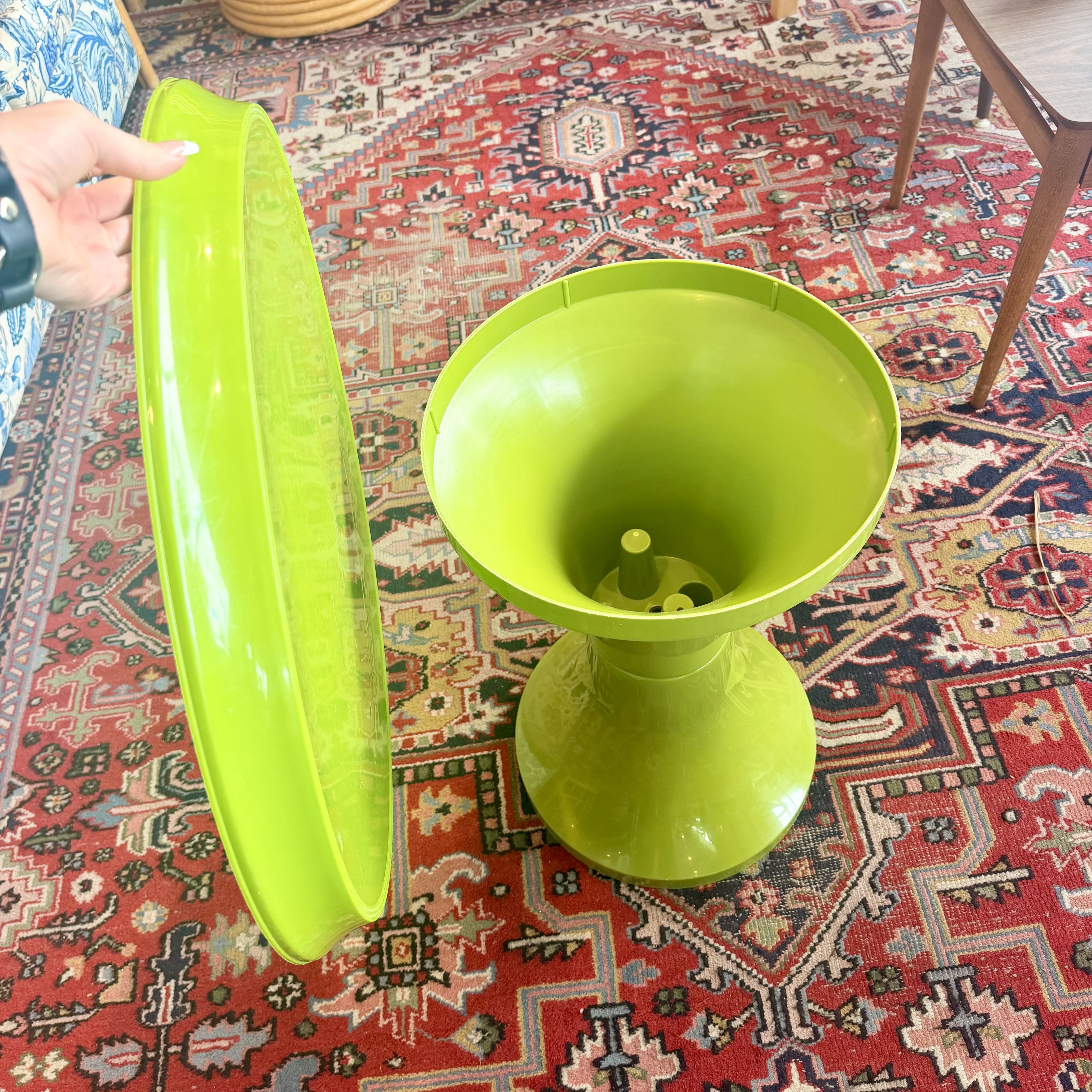 A bright lime green pedestal side table with a matching lid, shown on a red patterned oriental rug with a hand holding the lid.