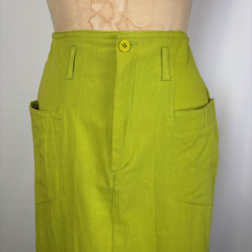 A close-up of a bright yellow-green skirt or trouser leg on a mannequin torso, showing front pockets, belt loops, and a yellow button closure against a plain light background.