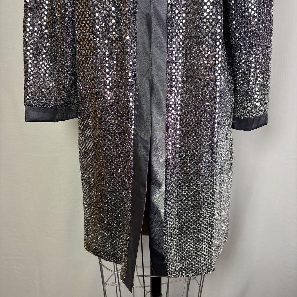 A long black satin-trimmed jacket covered in dense silver sequins, displayed on a wire dress form against a light gray fabric backdrop.