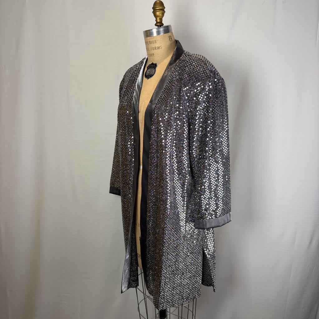 A silver sequined open-front cardigan or kimono jacket displayed on a tan dress form mannequin against a light gray fabric backdrop.