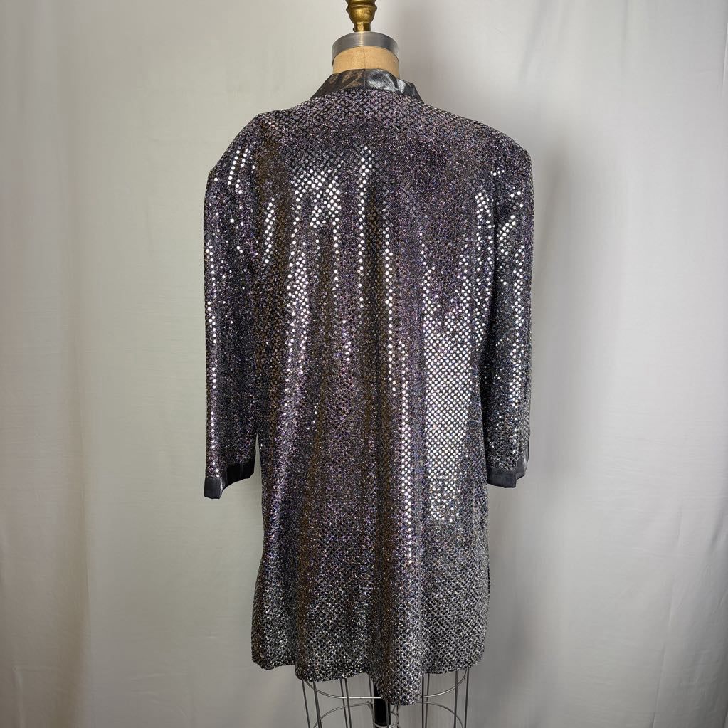 A long-sleeve, high-neck sequined jacket or tunic displayed on a dress form against a light gray fabric backdrop.