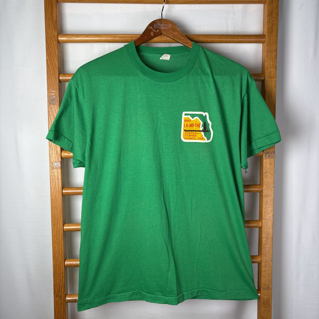 A green t-shirt with a small Florida logo that reads Camp La-No-Che on a wooden rack.