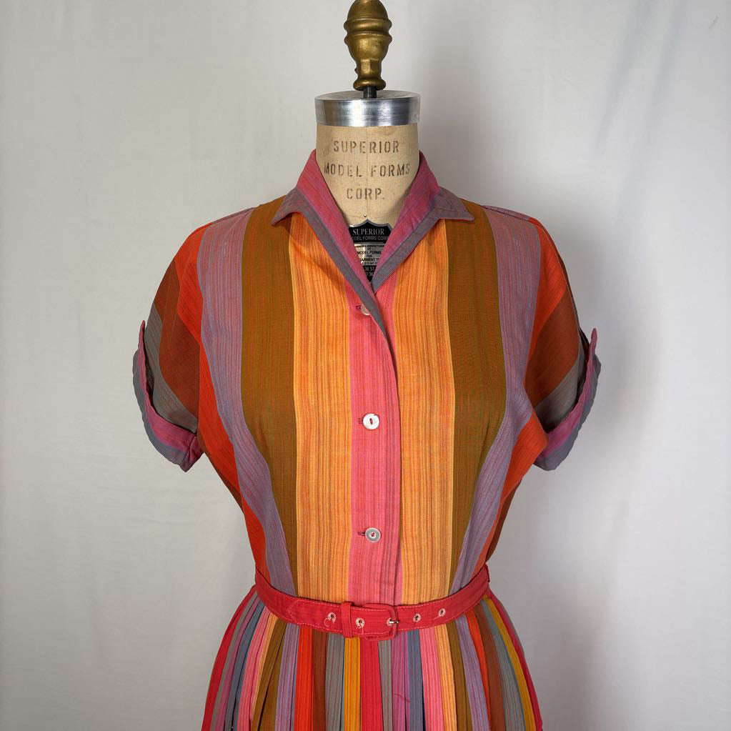 A short-sleeve collared shirt dress displayed on a vintage model form. The dress features vertical stripes in orange, pink, red, purple, and blue, with a matching red belt at the waist.