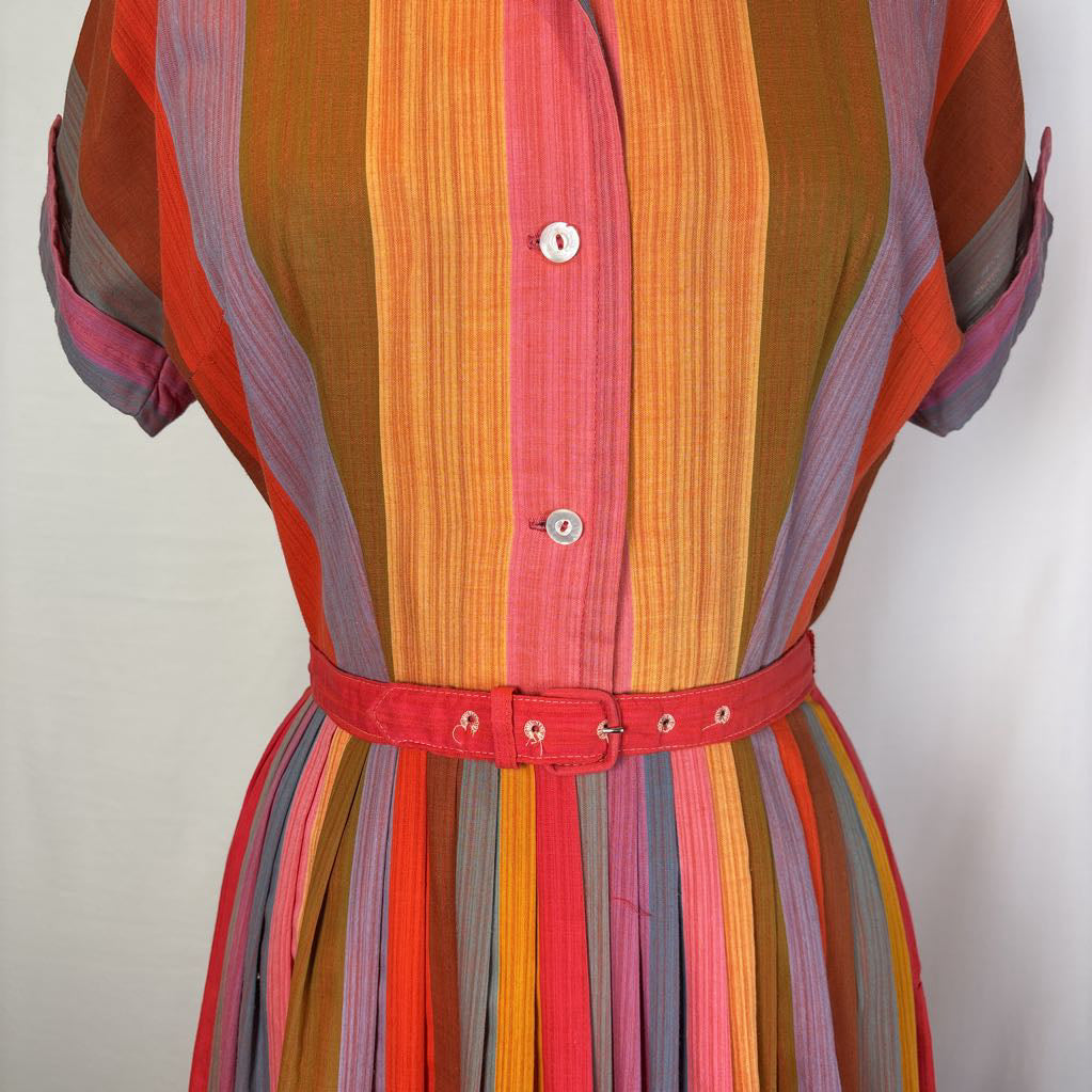 A close-up of a vintage-style striped dress featuring vertical stripes in orange, pink, red, brown, and purple, with a matching red belt at the waist.