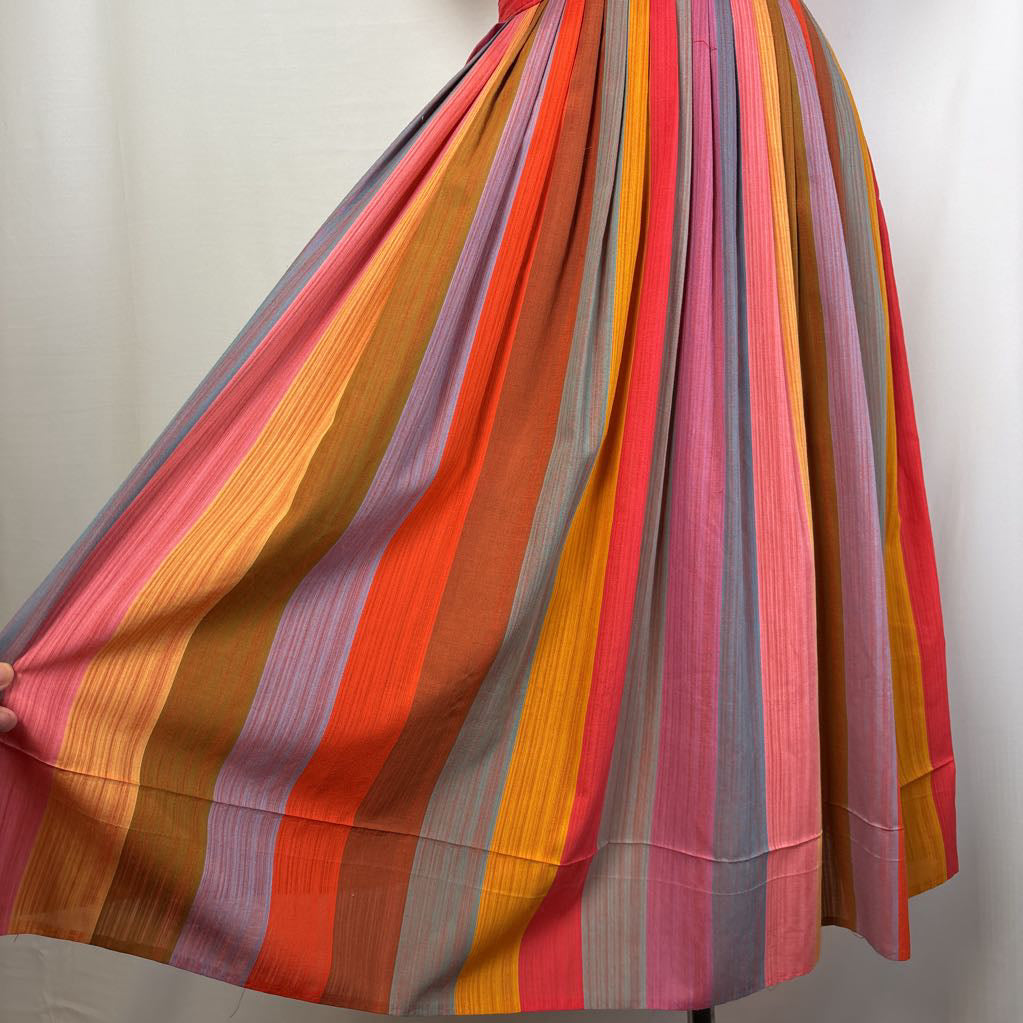 A pleated skirt with vertical stripes in orange, pink, red, yellow, brown, and gray, displayed on a mannequin against a white background.