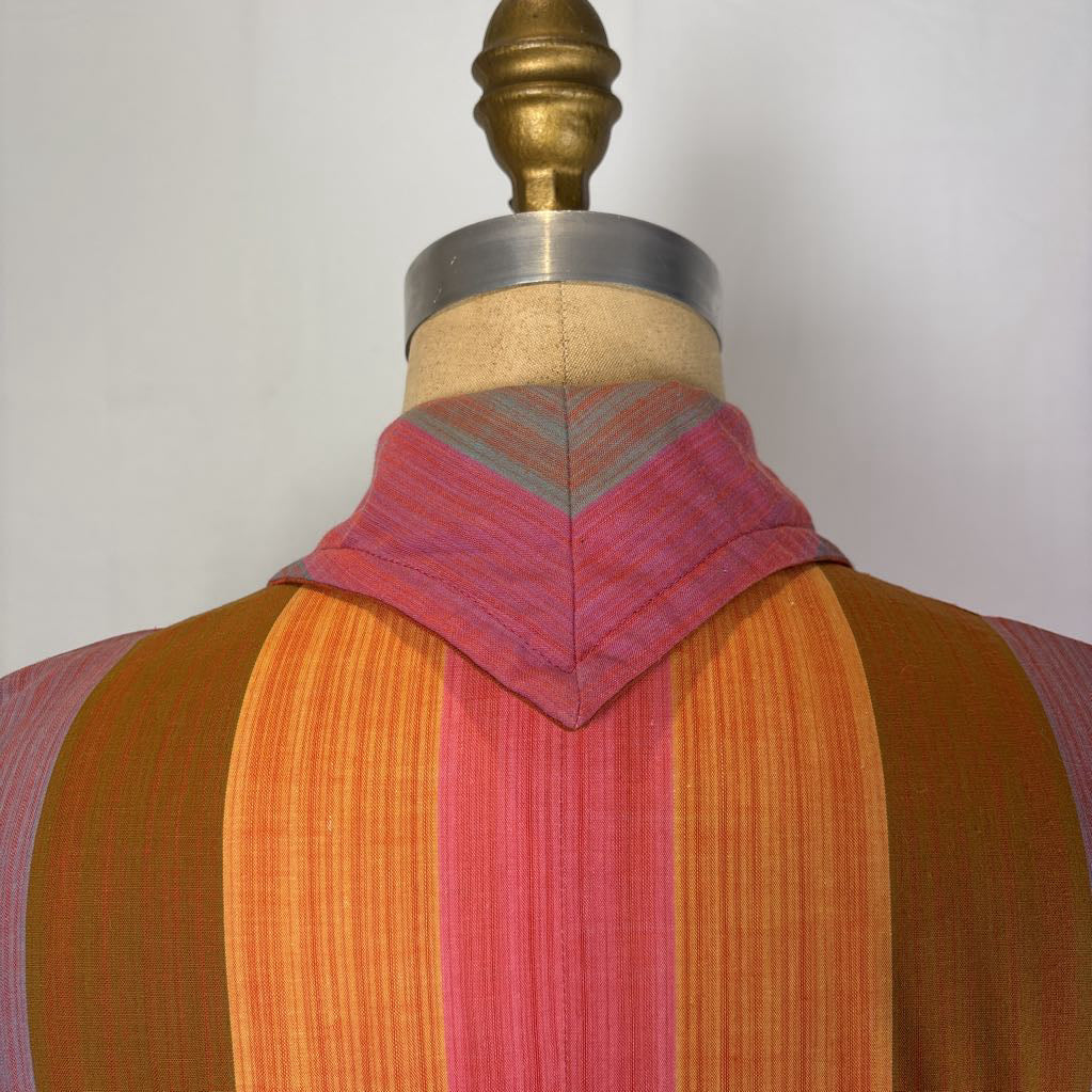 A close-up of a striped garment displayed on a dress form mannequin against a plain light background. The fabric features vertical stripes in orange, pink, brown, and purple, with a matching striped collar.