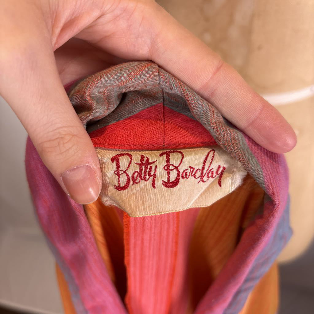 A close-up of a hand holding open a colorful garment to reveal an embroidered 'Bottt Barclay' label inside.