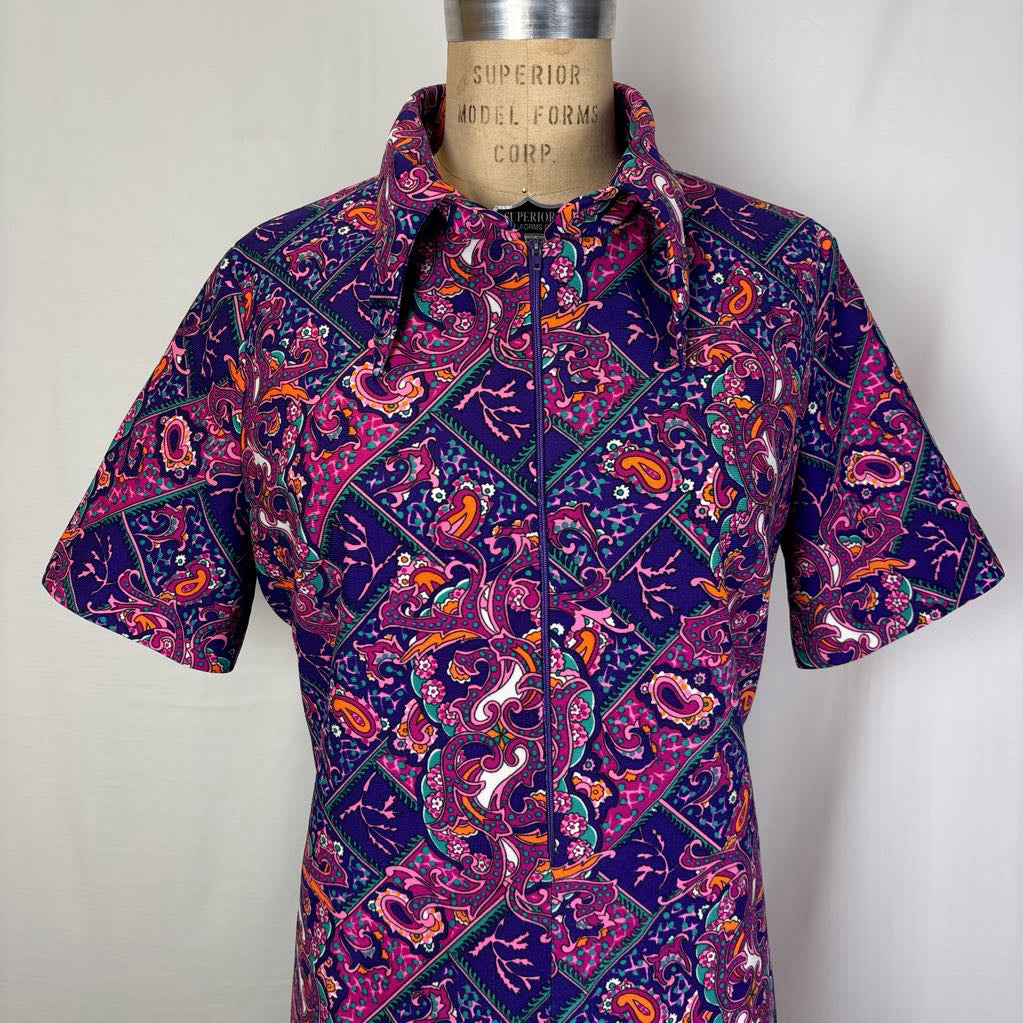 A short-sleeve collared button-up shirt with a colorful paisley and diamond pattern, displayed on a vintage wooden mannequin torso against a plain light background.