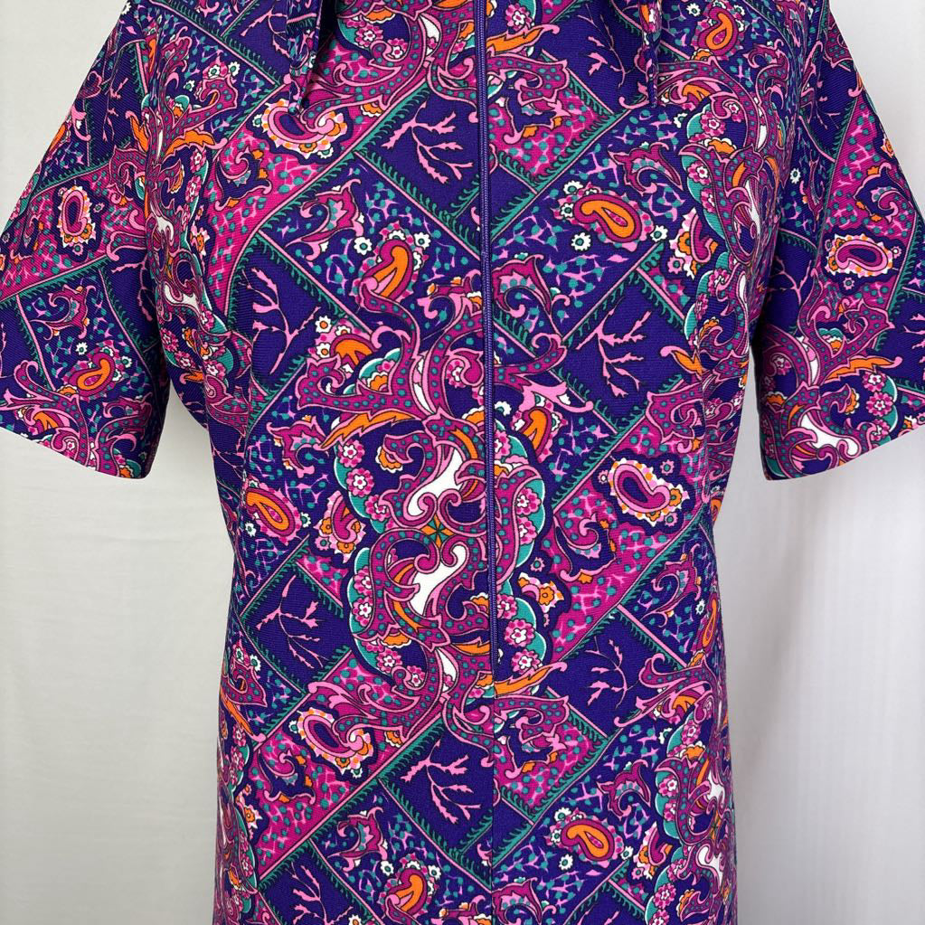 A short-sleeve button-up shirt with a vibrant purple, pink, and orange paisley batik pattern, displayed on a white background.