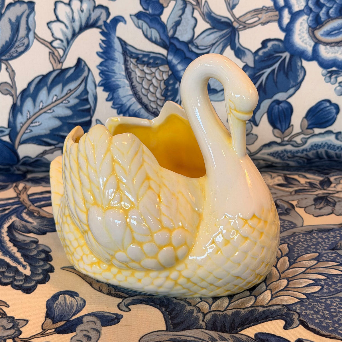 A yellow and cream-colored ceramic swan figure on a blue and white fabric surface.