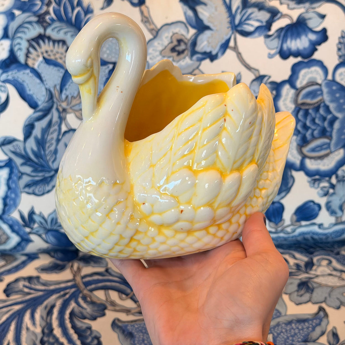 A yellow and cream-colored ceramic swan figure on a blue and white fabric surface.