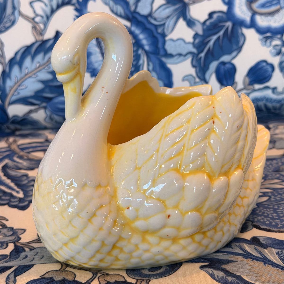 A yellow and cream-colored ceramic swan figure on a blue and white fabric surface.