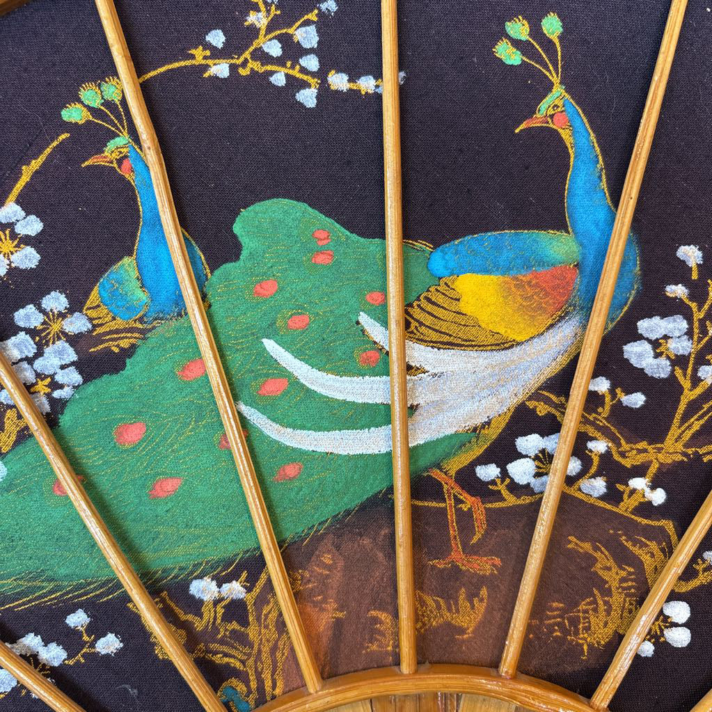 A black fabric and wooden fan wall decor with a painted peacock motif.