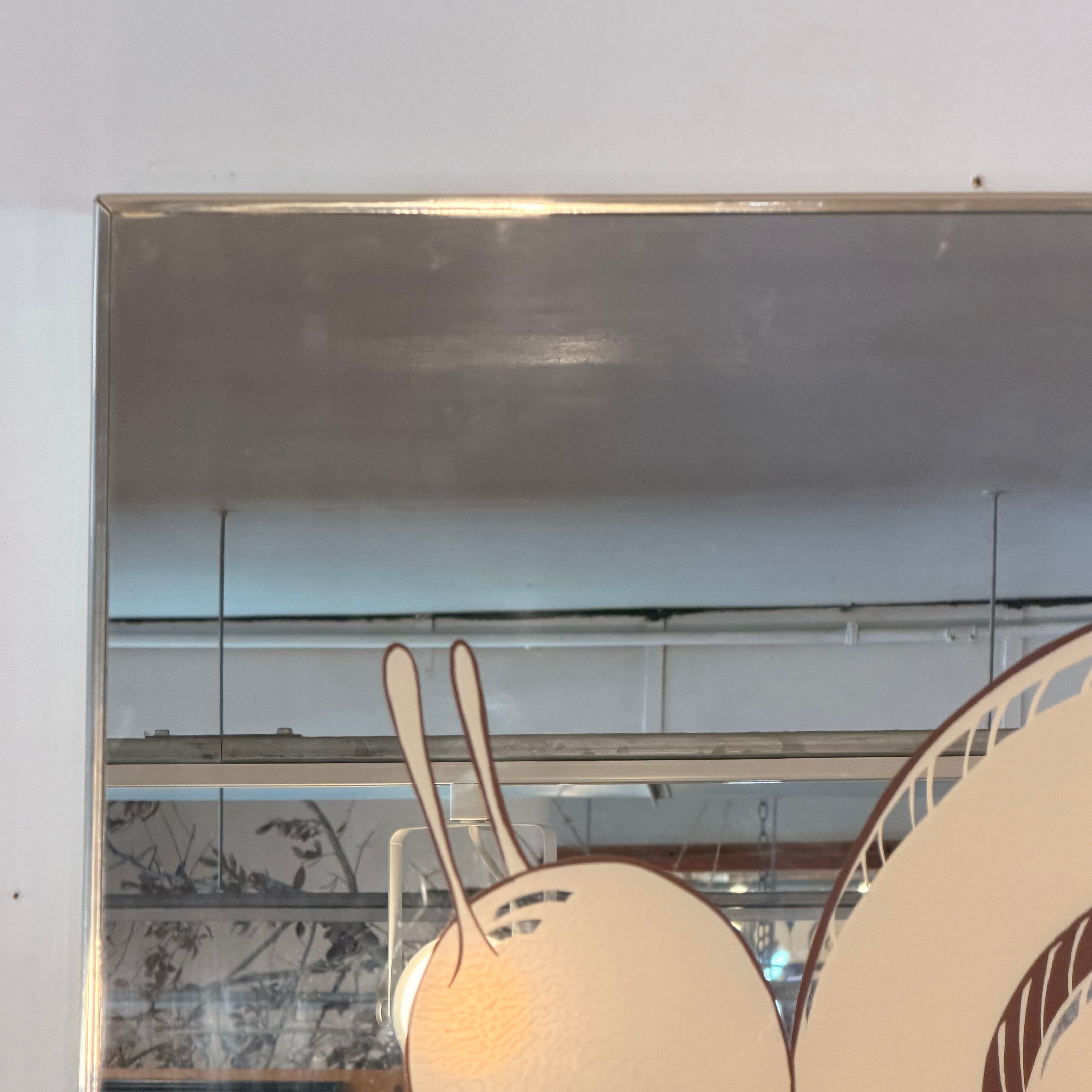 A square wall mirror with a thin metallic frame, reflecting an indoor ceiling and light fixture. In the foreground, a stylized cream-colored rabbit silhouette with brown outlines is partially visible at the bottom.