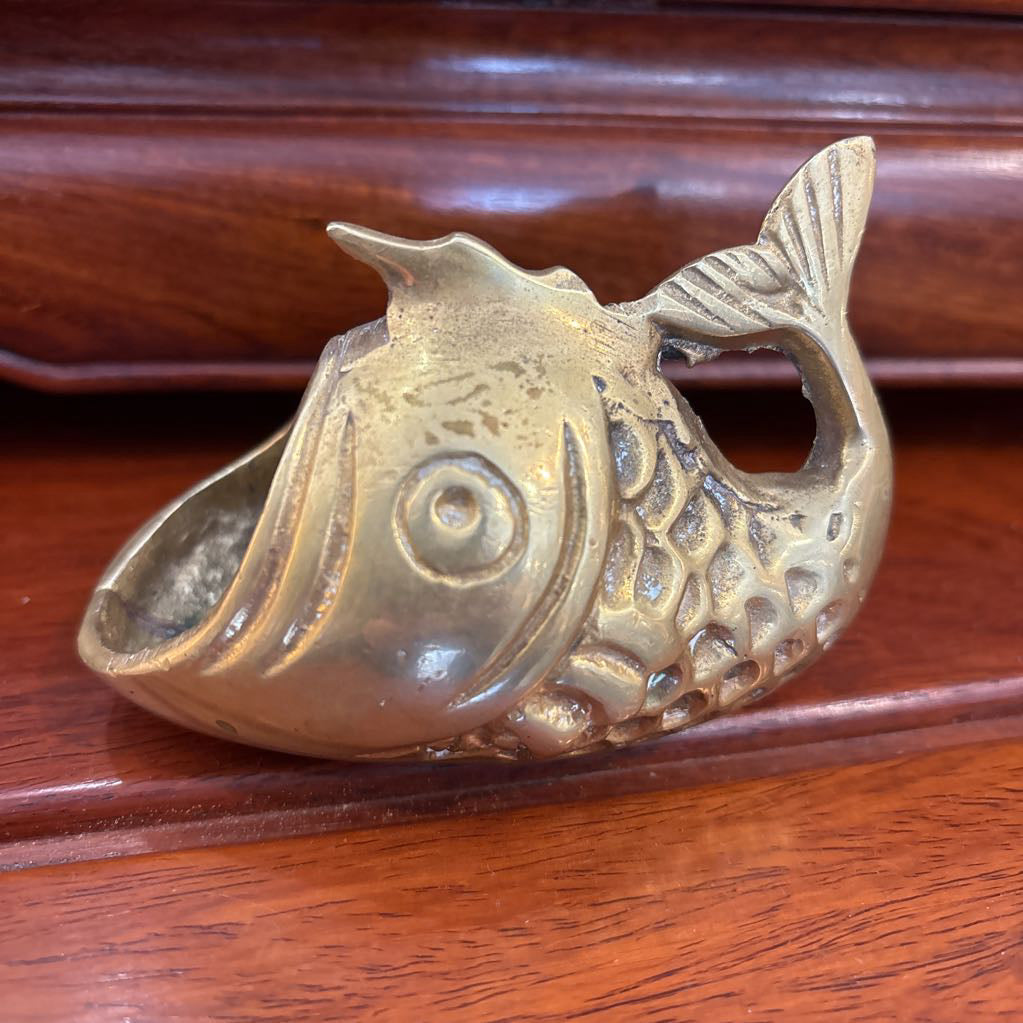 A brass fish figure with its mouth wide open on a brown wooden surface.