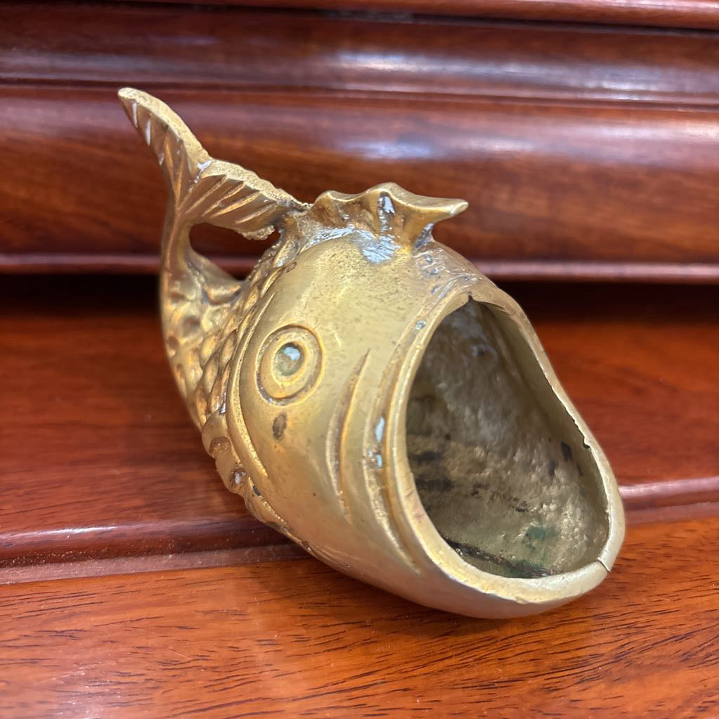 A brass fish figure with its mouth wide open on a brown wooden surface.