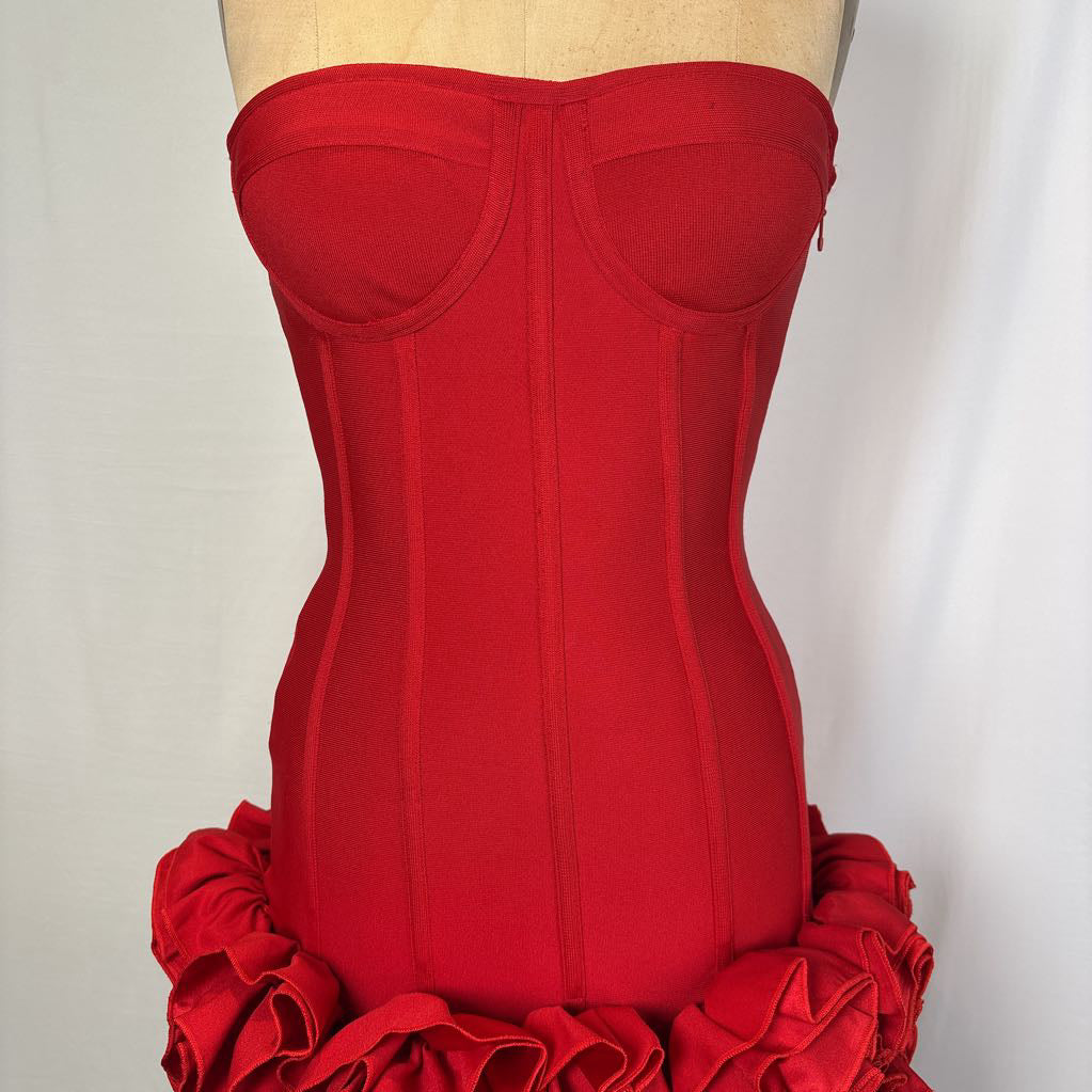 A bright red strapless corset-style dress bodice displayed on a mannequin torso against a plain light background. The bodice has structured cup shapes, vertical seam detailing, and a ruffled red skirt or hem visible at the bottom.