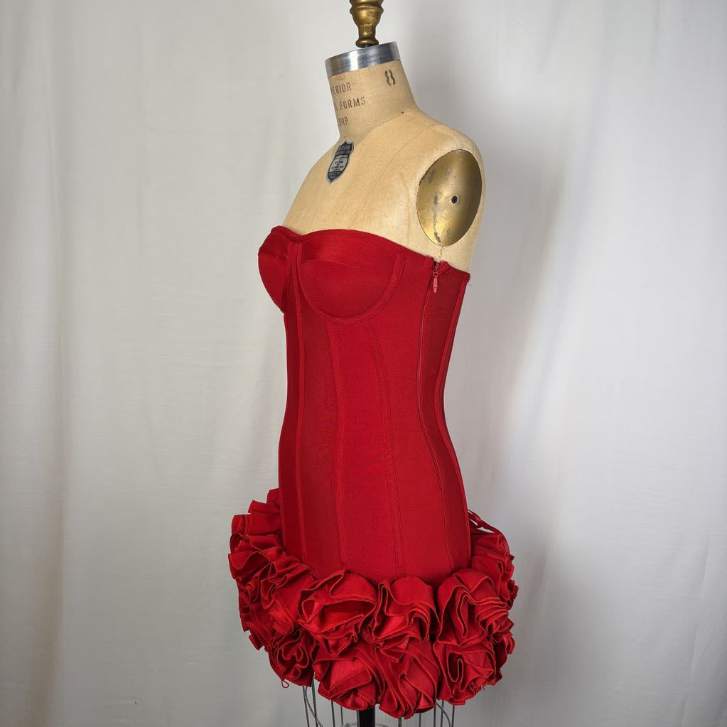 A red strapless corset-style dress displayed on a wooden dress form against a white curtain background.