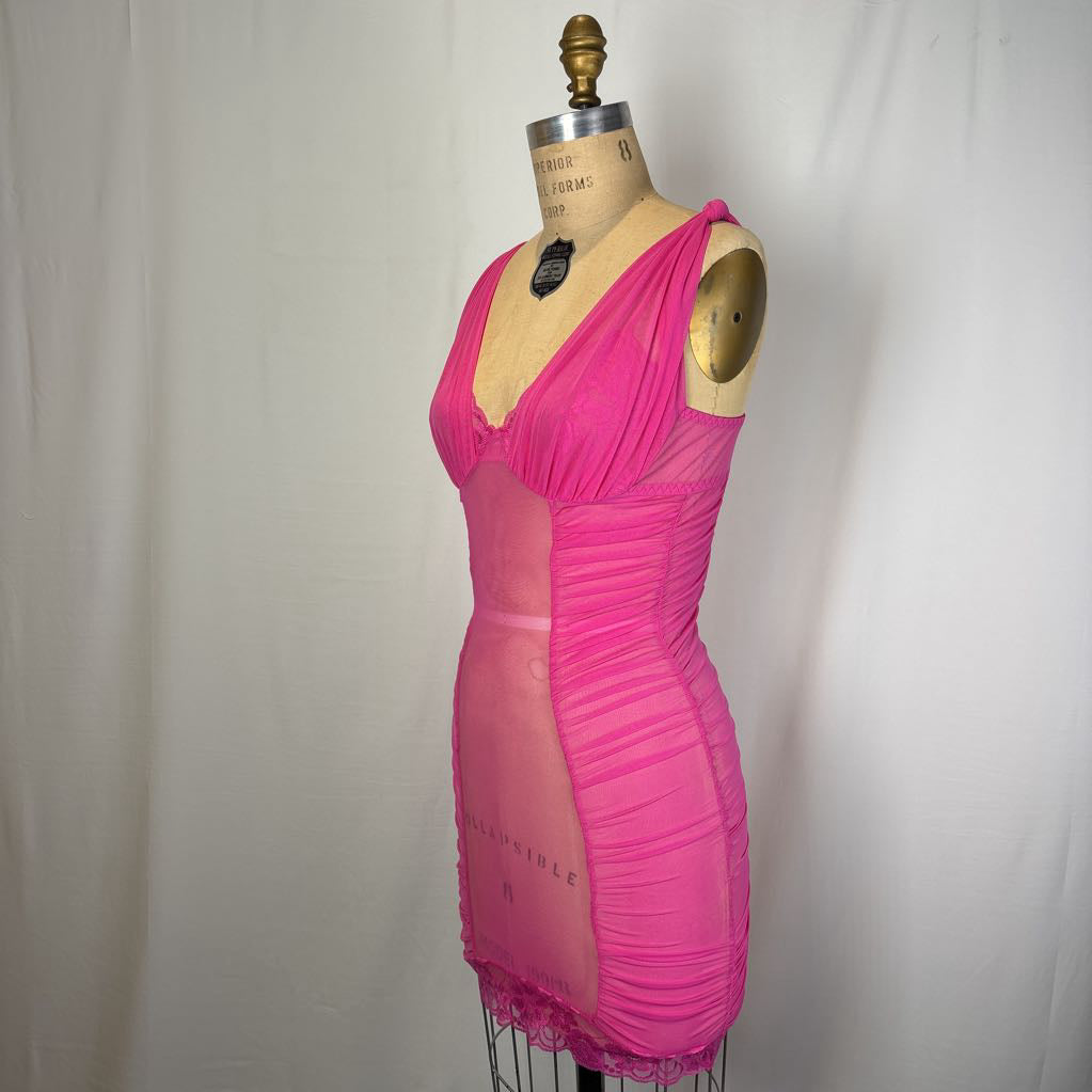 A bright pink vintage-style sheer mesh and ruched dress displayed on a wooden dress form mannequin against a white fabric backdrop.