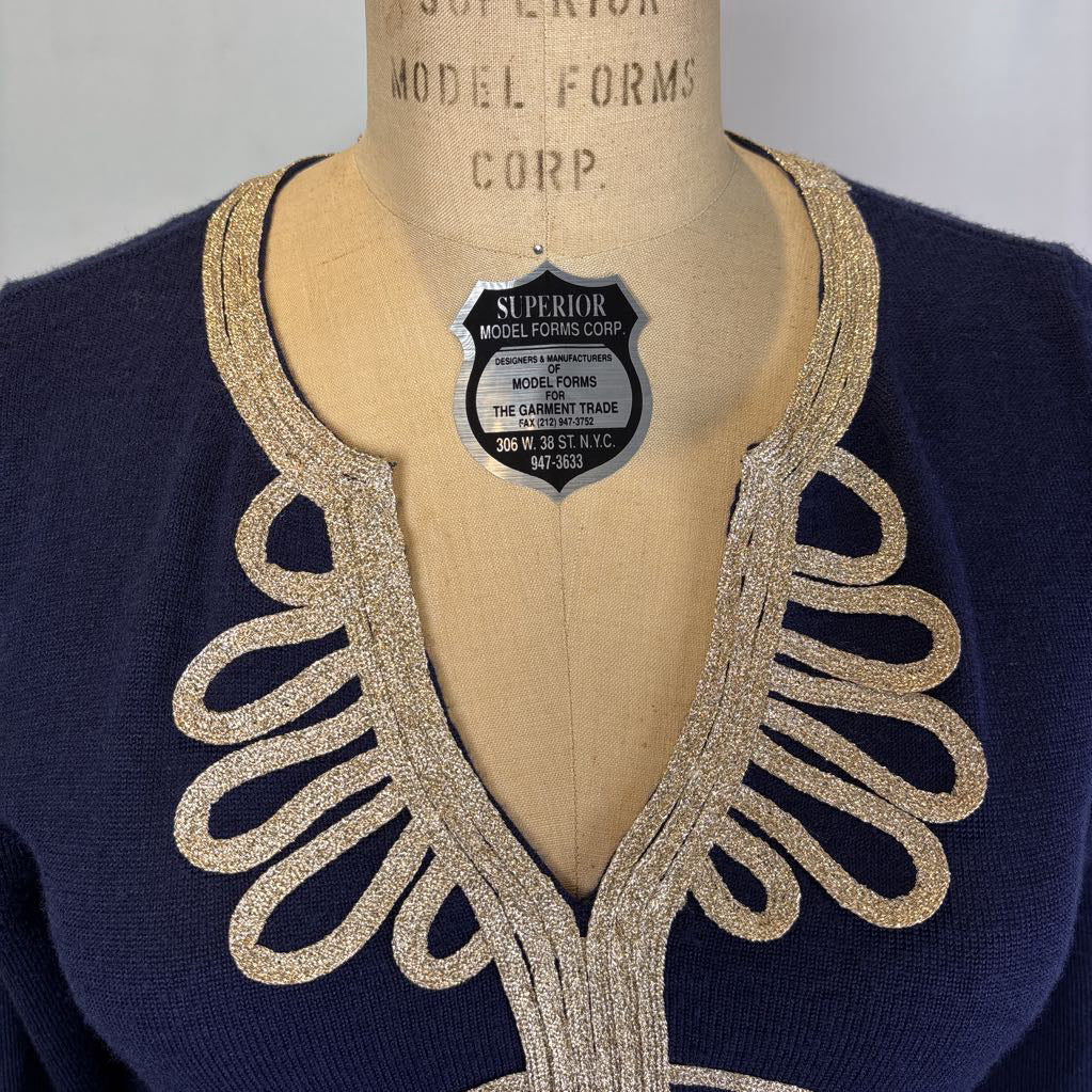 A navy blue knit sweater displayed on a vintage tan mannequin torso, featuring a large, ornate glittery gold V-neckline trim. A silver 'Superior Model Forms Corp.