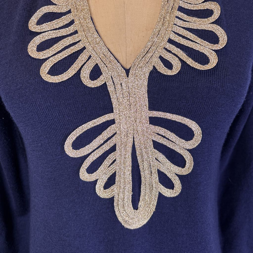 Close-up of a navy blue knit sweater with a large, ornate V-neckline detail in a shimmering champagne-gold metallic fabric, displayed on a mannequin torso.
