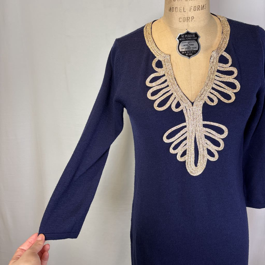 A navy blue long-sleeve tunic dress displayed on a vintage wooden dress form. The dress features a deep V-neckline embellished with a large, symmetrical cream-colored embroidered pattern.