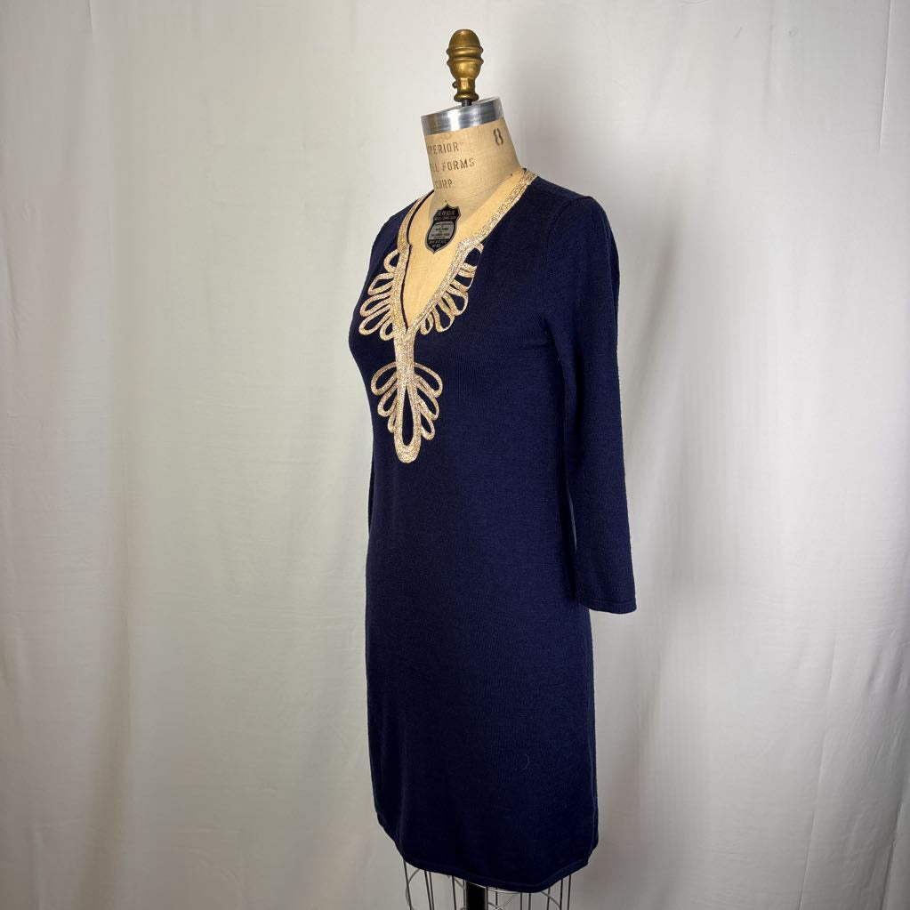 A navy blue knit tunic dress with a beige embroidered floral pattern around the V-neck, displayed on a dress form mannequin against a white fabric backdrop.