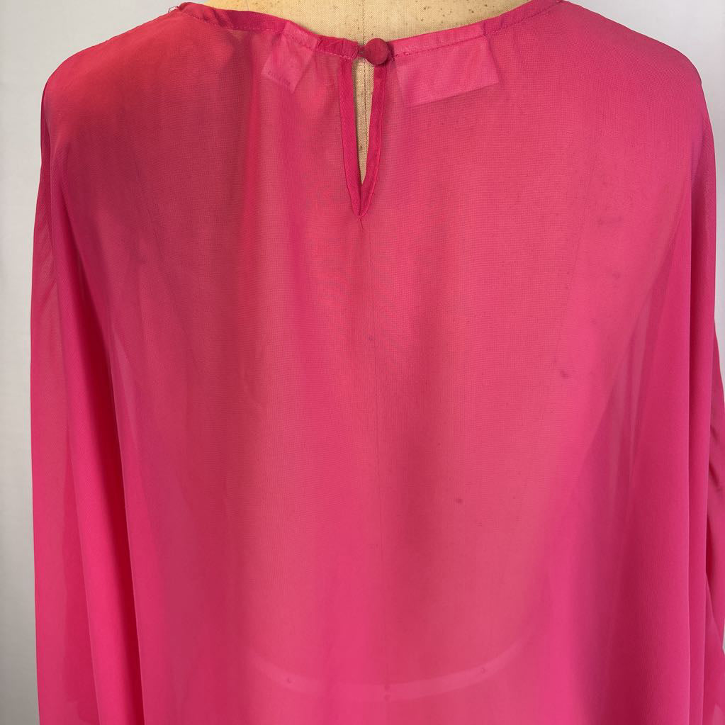 A bright pink long-sleeve blouse displayed on a dress form, showing the back view with a keyhole cutout and a decorative button closure.
