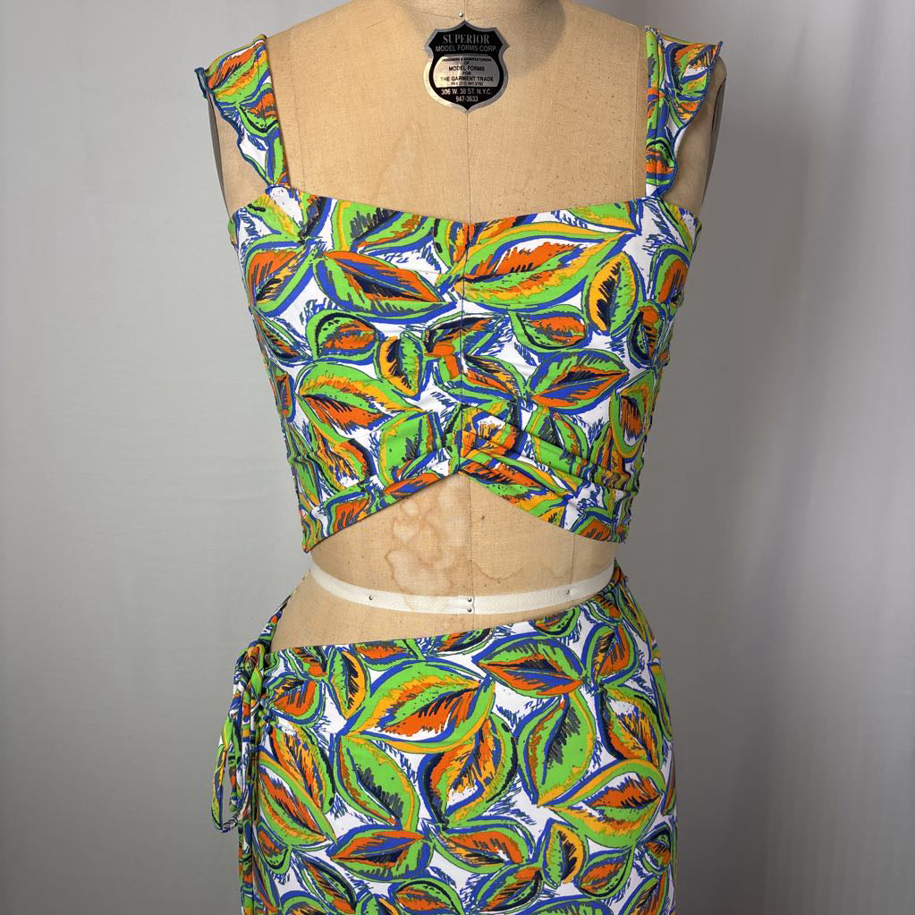 A two-piece matching set consisting of a sleeveless crop top and a high-waisted skirt, both featuring a vibrant multicolor leaf print on a white background. The set is displayed on a tan dress form mannequin against a neutral gray background.