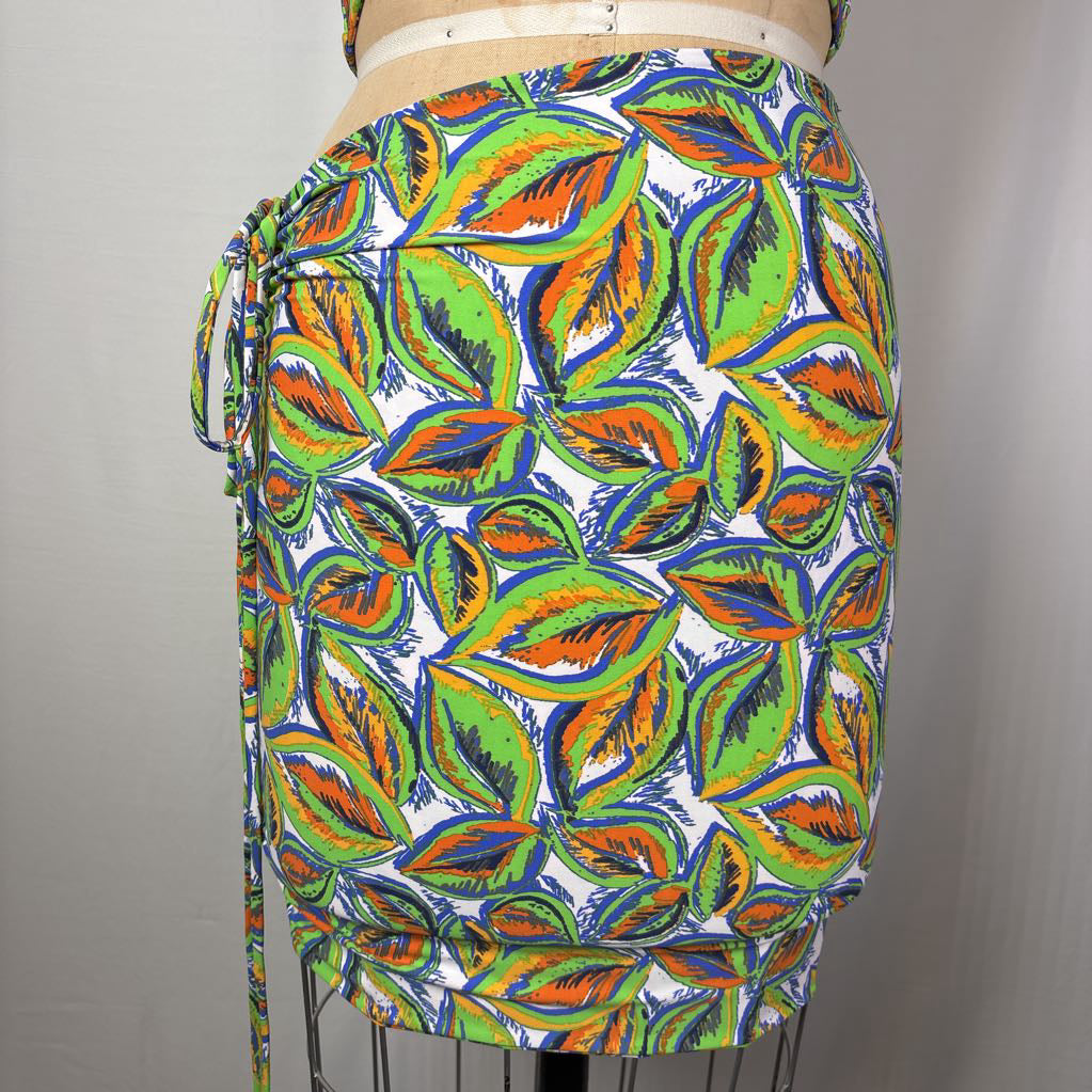 A multicolor tropical leaf print wrap skirt displayed on a dress form mannequin against a neutral gray background.