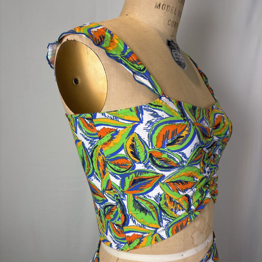 A vintage-style sleeveless top with a colorful leaf print, displayed on a wooden dress form mannequin against a plain light gray background.