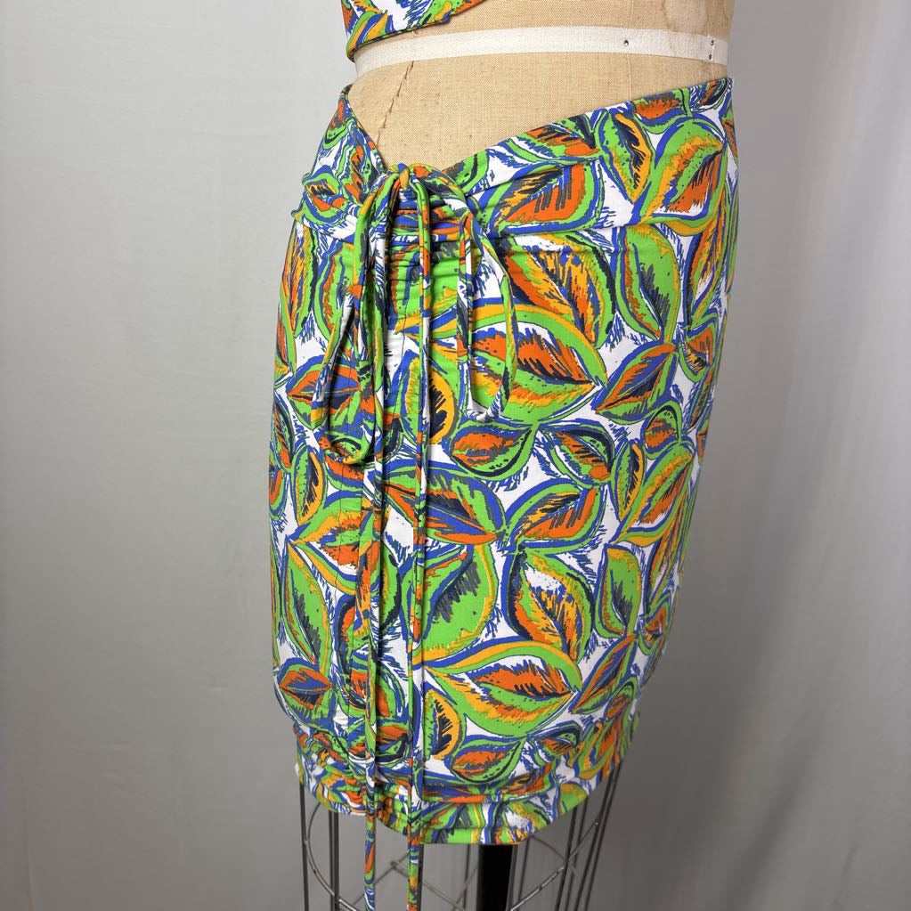 A multicolor African wax print skirt with a green and orange leaf pattern, displayed on a dress form mannequin against a neutral gray background.