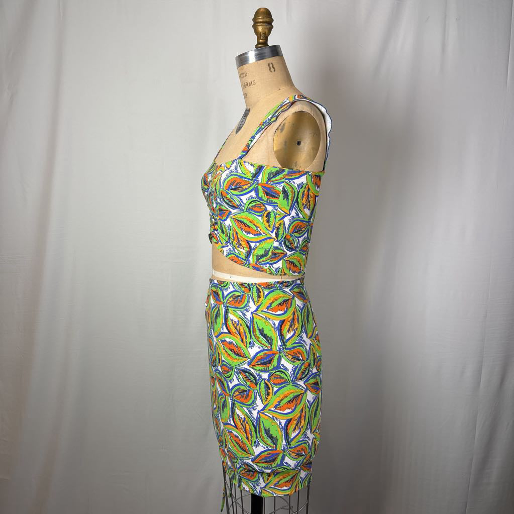 A sleeveless two-piece set with a matching crop top and pencil skirt, featuring a vibrant multicolor abstract leaf pattern in green, orange, yellow, and blue on a white background, displayed on a dress form.
