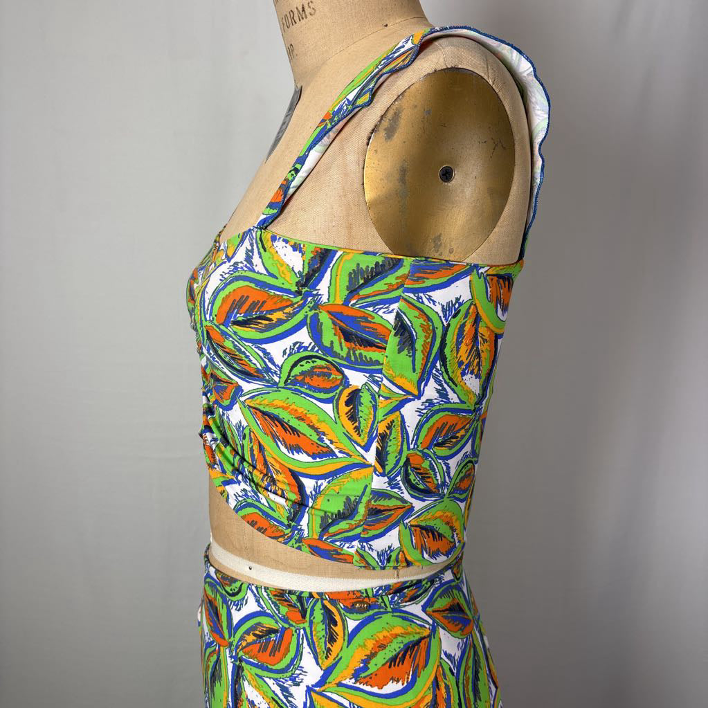 A two-piece matching set featuring a sleeveless crop top and skirt with a vibrant multicolor leaf pattern, displayed on a vintage wooden dress form mannequin against a neutral gray background.