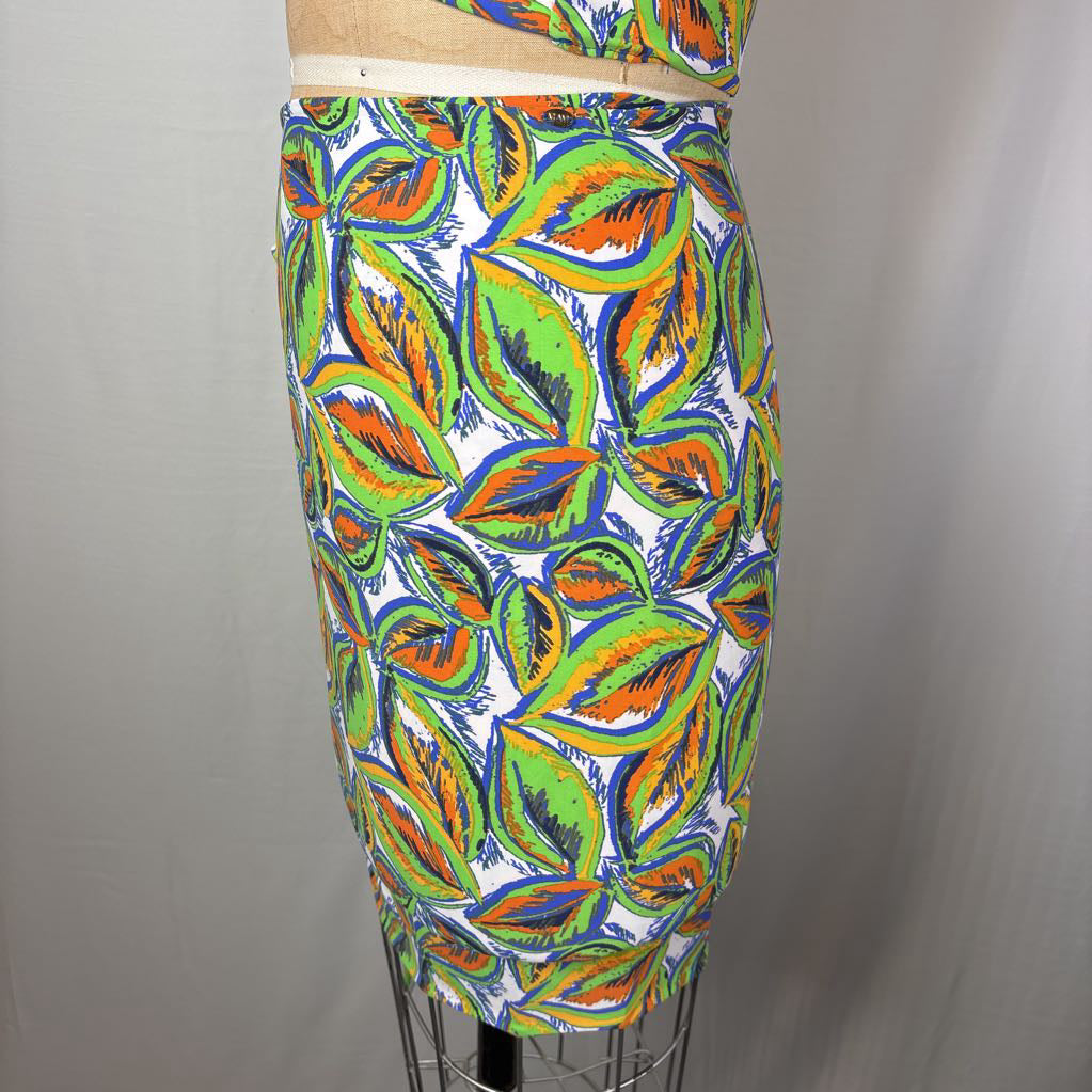 A fitted pencil skirt with a vibrant, multicolor abstract leaf pattern on a white background, displayed on a dress form mannequin against a neutral gray backdrop.