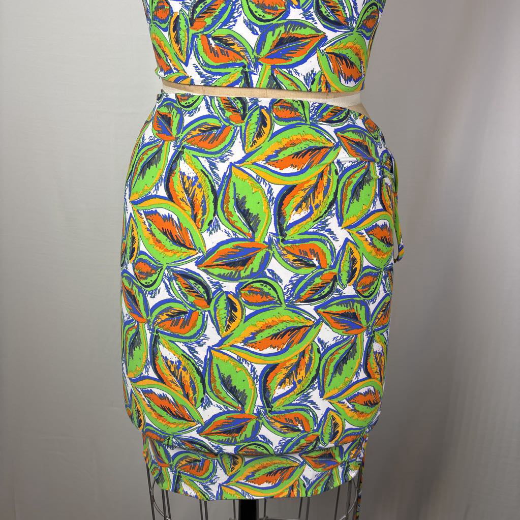 A two-piece matching set consisting of a sleeveless crop top and a fitted pencil skirt, both featuring a vibrant, hand-drawn style leaf pattern in green, orange, blue, and yellow on a white background, displayed on a dress form.