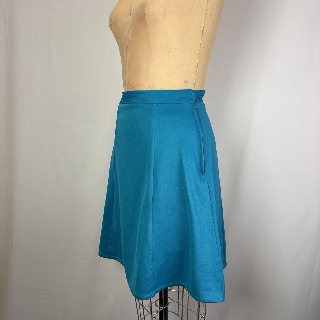 A teal blue A-line skirt displayed on a tan dress form mannequin against a white fabric backdrop.