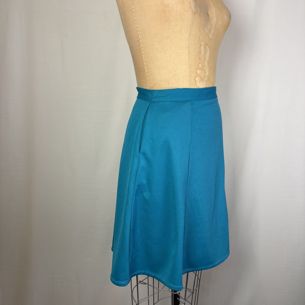 A bright teal blue A-line skirt displayed on a tan dress form mannequin against a light gray fabric backdrop.