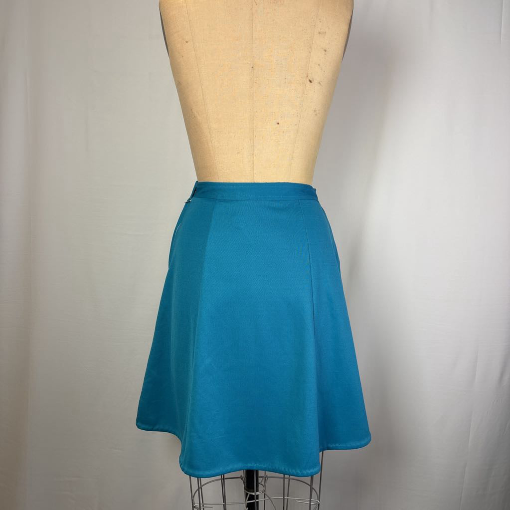 A bright teal blue A-line skirt displayed on a tan dress form mannequin against a white fabric backdrop.
