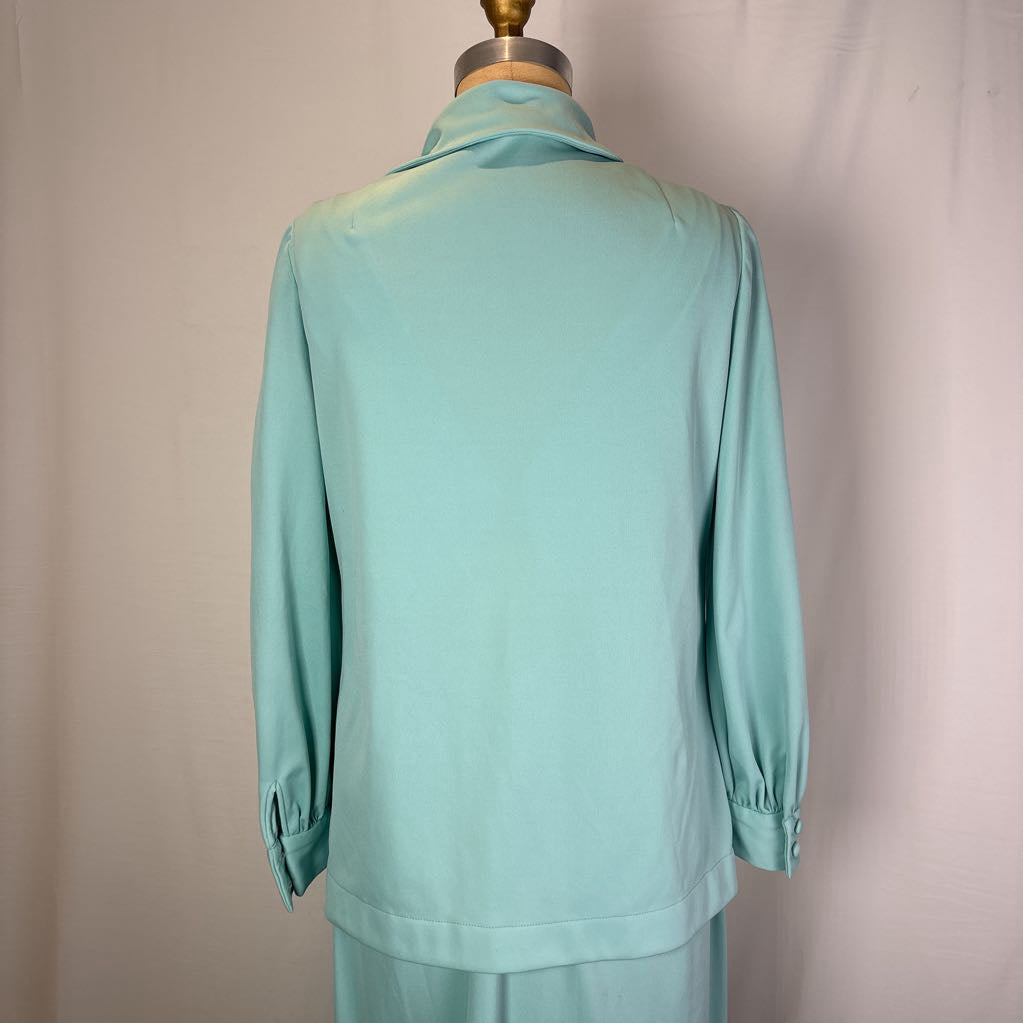A mint green long-sleeve blouse displayed on a dress form from the back, featuring a high folded collar and gathered elbow-length sleeves with button details.