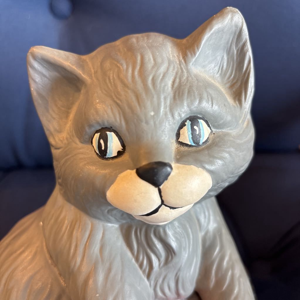 A ceramic figure of a gray cat sitting on a plush navy cushion. 
