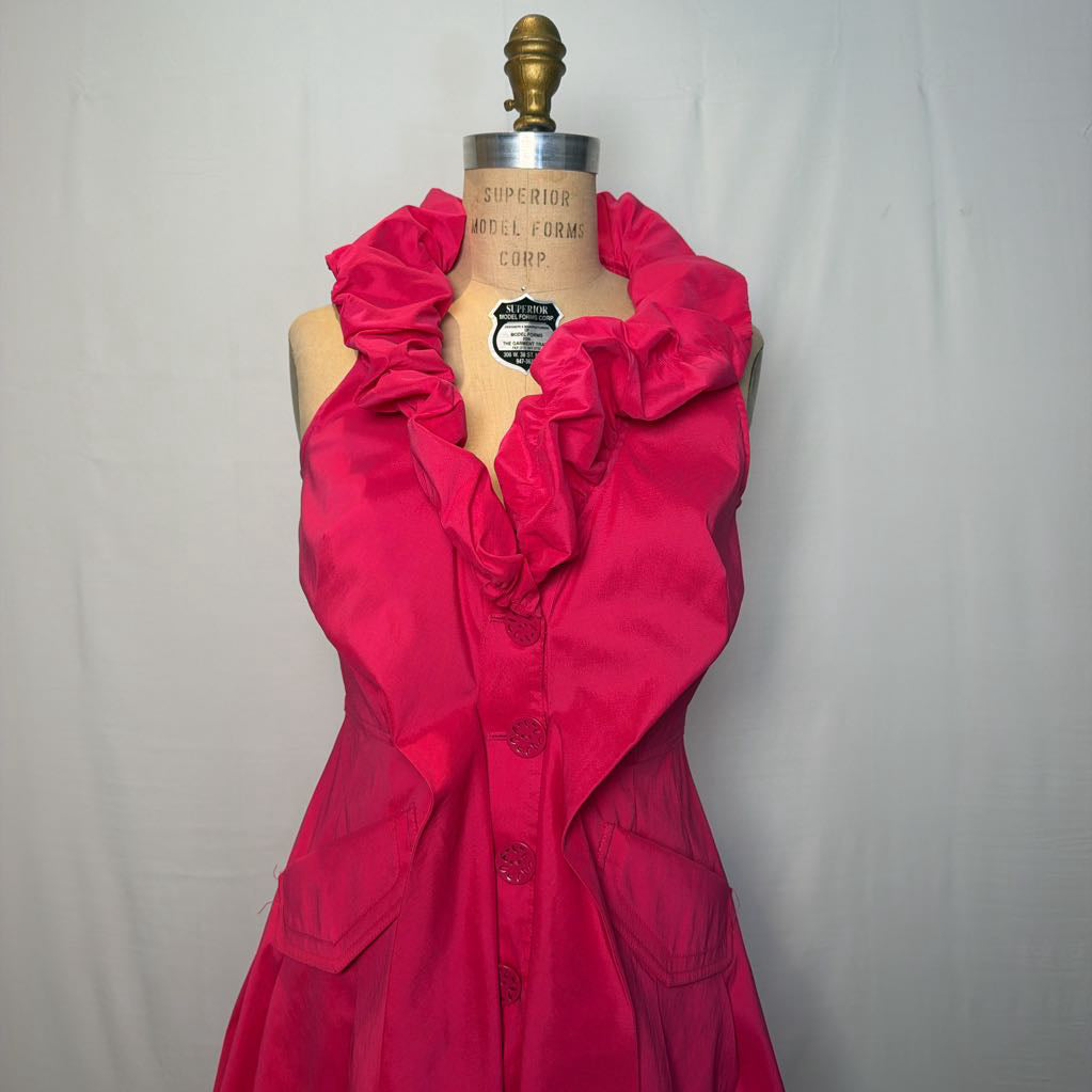 A bright pink button-up sleeveless dress with a ruffle collar on a mannequin in front of a white wall.