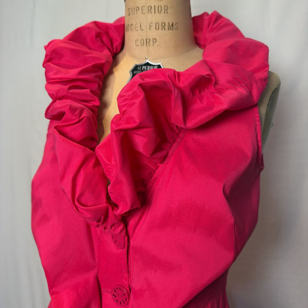 A bright pink button-up sleeveless dress with a ruffle collar on a mannequin in front of a white wall.