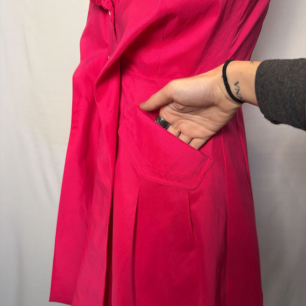 A bright pink button-up sleeveless dress with a ruffle collar on a mannequin in front of a white wall.