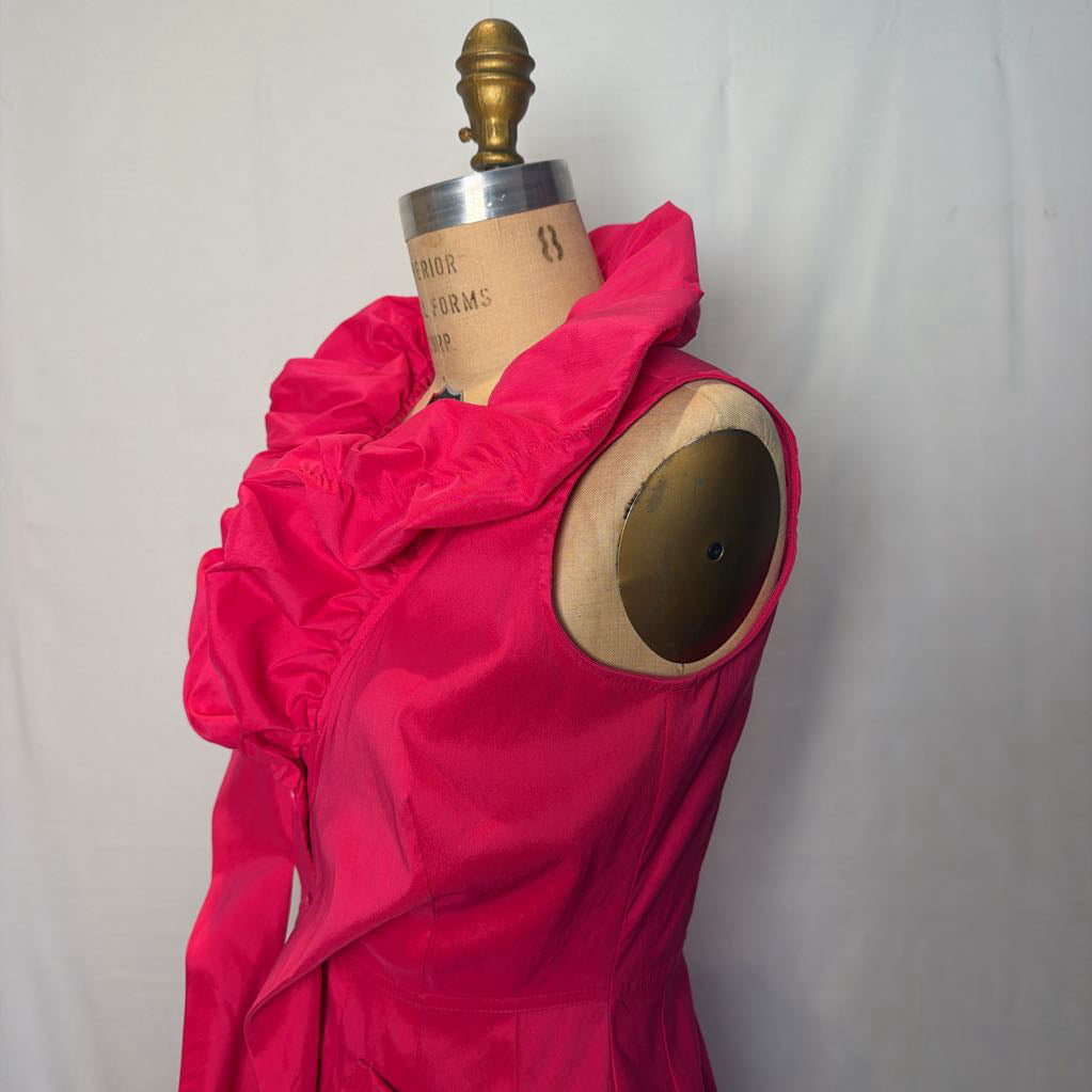 A bright pink button-up sleeveless dress with a ruffle collar on a mannequin in front of a white wall.
