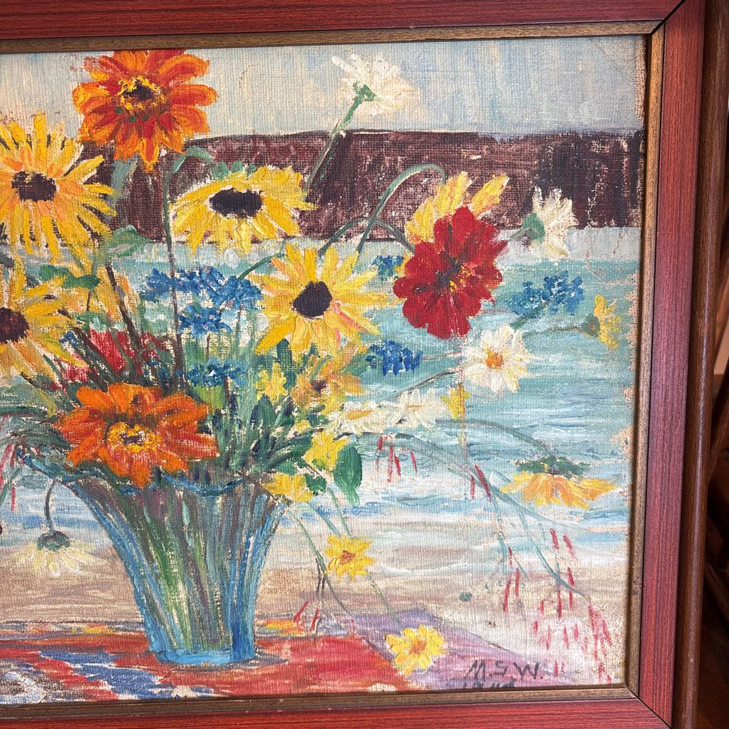 A framed still life of flowers in a vase on a wooden surface.