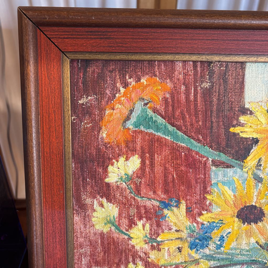 A framed still life of flowers in a vase on a wooden surface.
