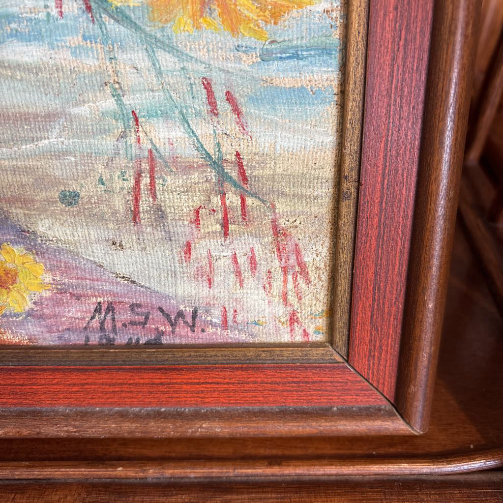 A framed still life of flowers in a vase on a wooden surface.